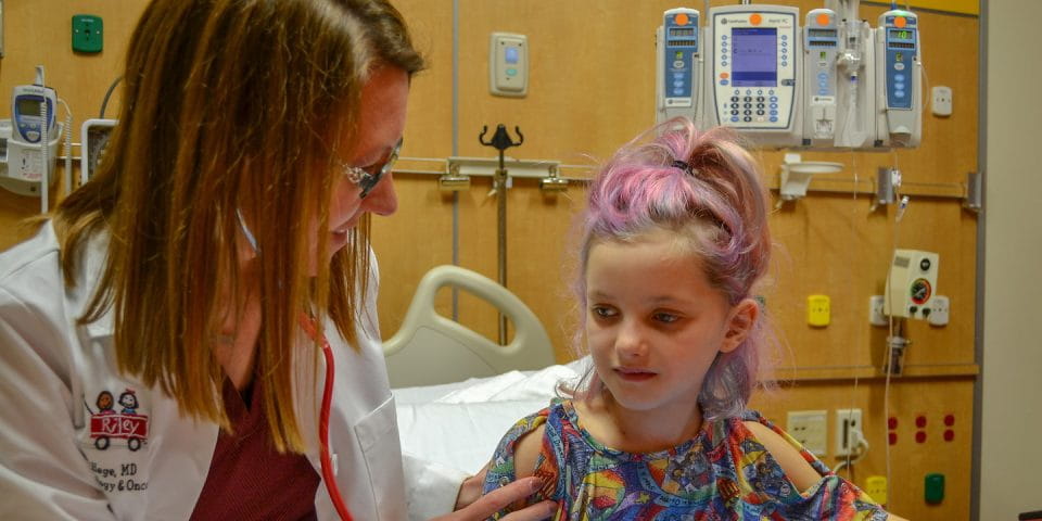 A female doctor interacts with a child patient in a hospital room.