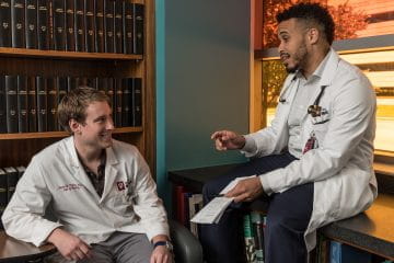 two Neurology residents talk in a library