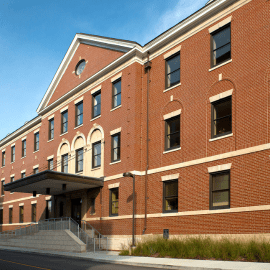Colored photograph of Coleman Hall, a brown brick building with a bright blue sky overhead