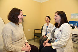 Two female doctors speak with a female patient in an exam room.