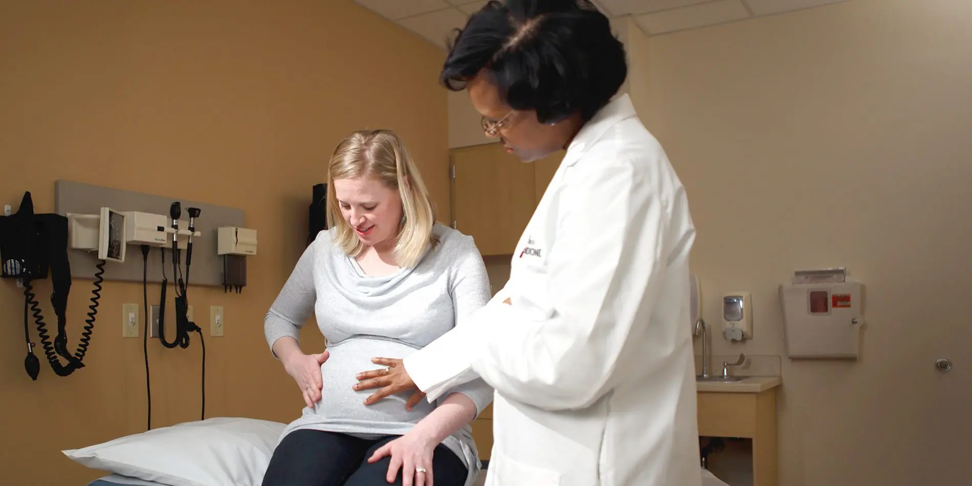A physician places her hand on the belly of a pregnant patient