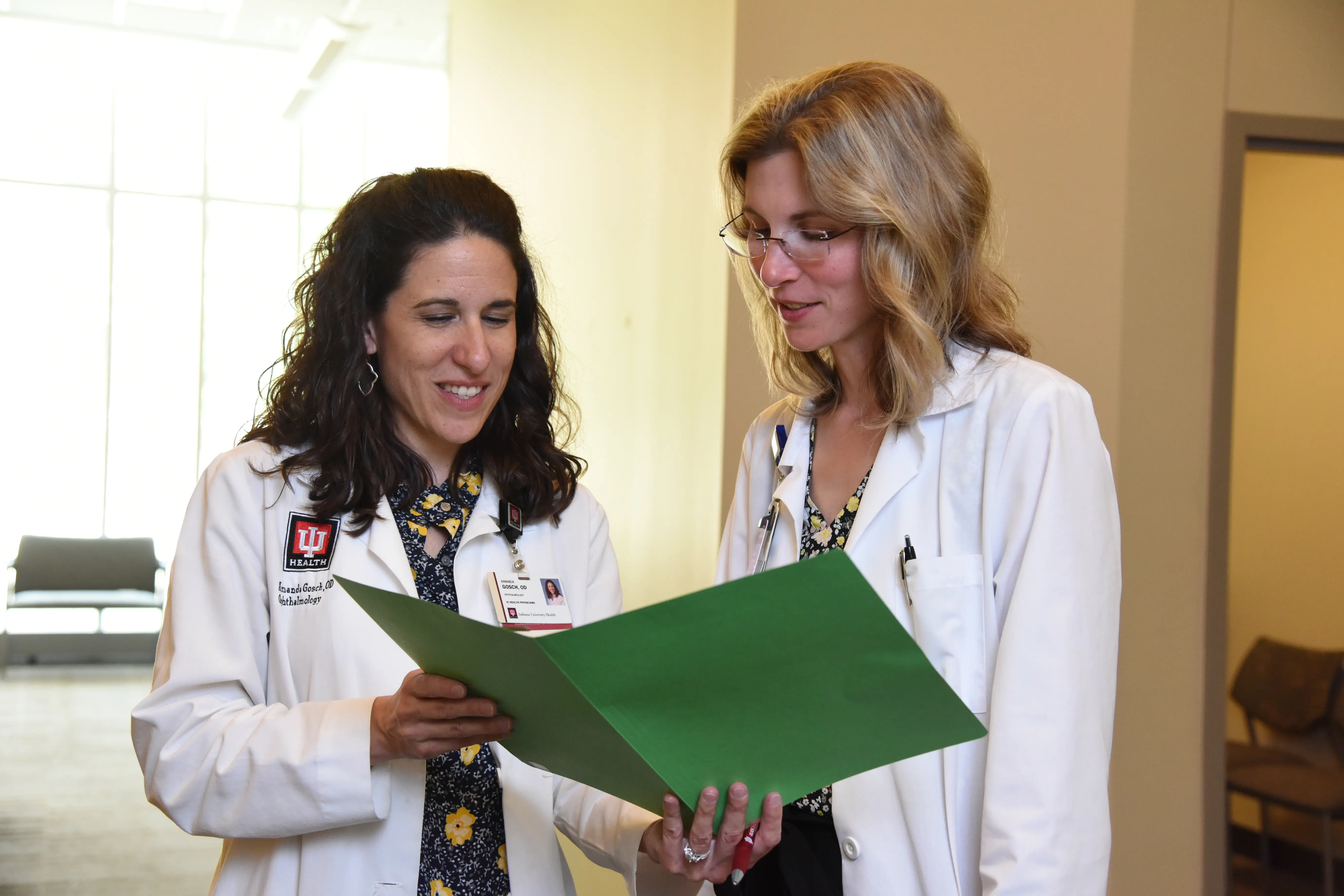 Drs. Amanda Gosch and Jennifer Eikenberry look over a patient file in a hallway of the Glick Eye Institute. 