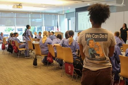 A female instructor from The Perry Initiative is shown wearing a t-shirt featuring a female surgeon and the phrase "We Can Do It!"