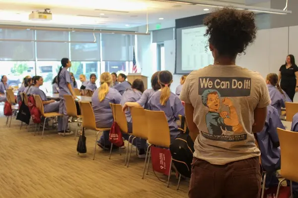 A female instructor from The Perry Initiative is shown wearing a t-shirt featuring a female surgeon and the phrase "We Can Do It!"