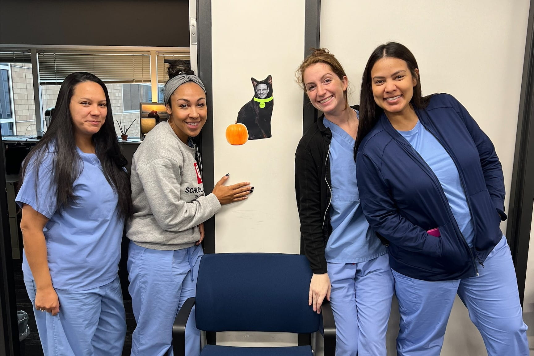 Four women stand in a hallway wearing scrubs.
