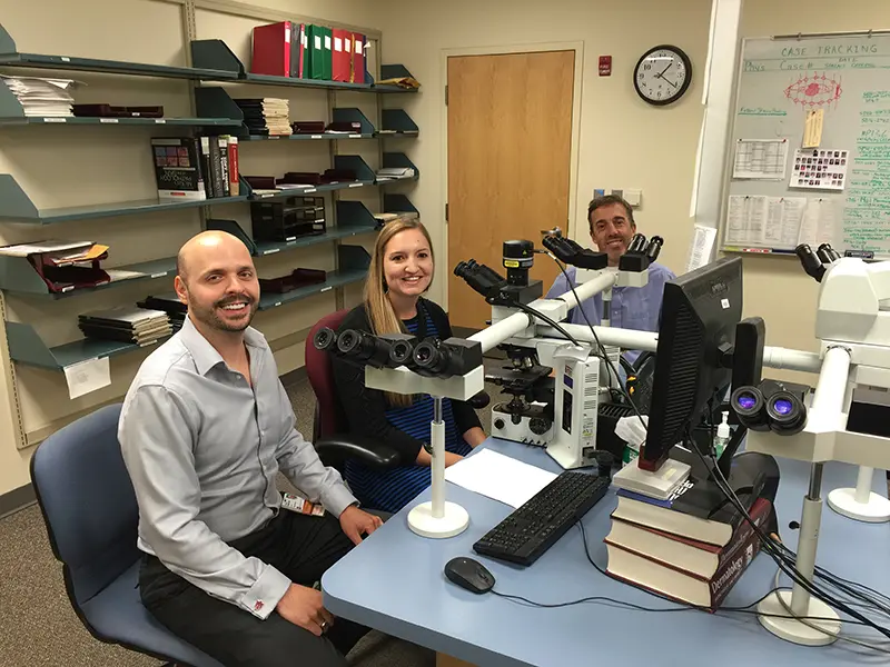 Christina Cole and her mentors sit in front of their microscopes in the path lab