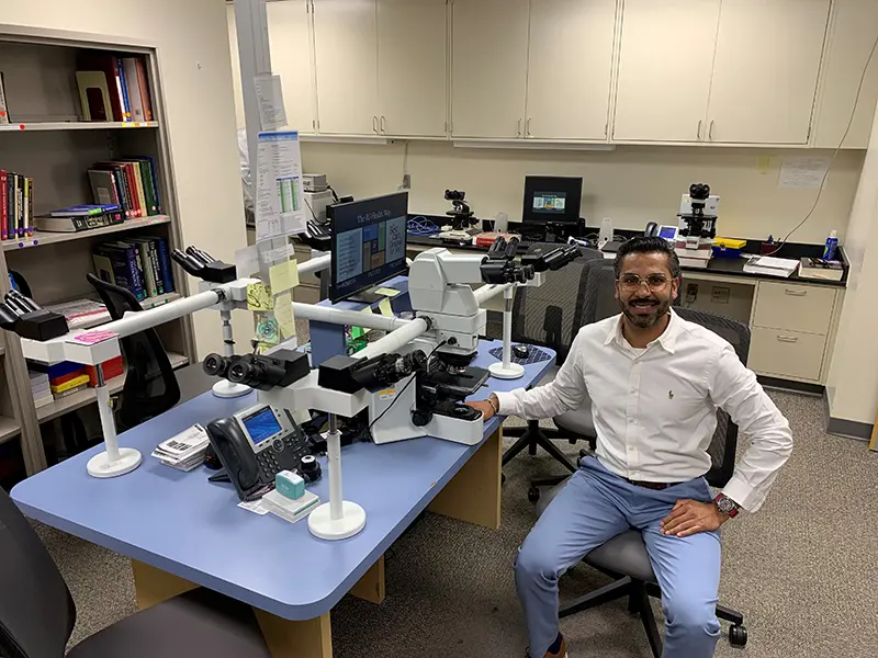 A pathologist sits in front of the microscopy table