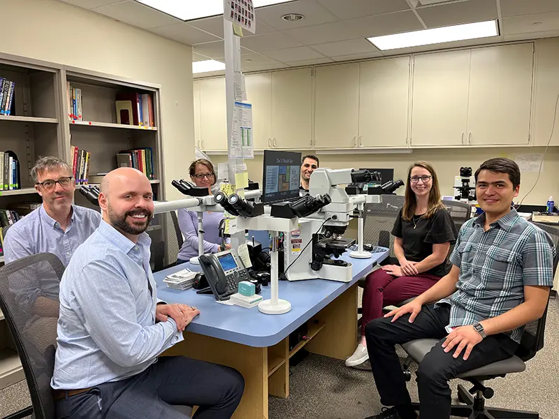 Six pathologists smile at the camera while sitting in front of their microscopes
