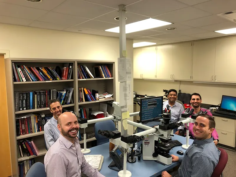 Five pathologists sit at a table filled with microscope equipment