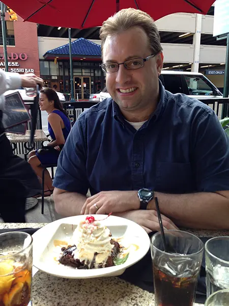 Paul Hillesheim sits at a cafe with a piece of cake on the table in front of him.