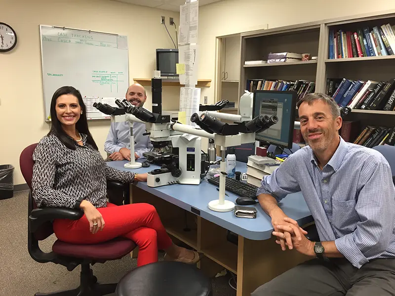 Three pathologists sit in front of their microscopes