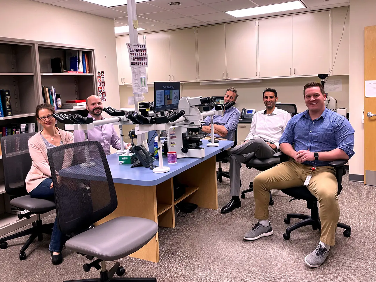 Five pathologists sit at a table filled with microscope equipment