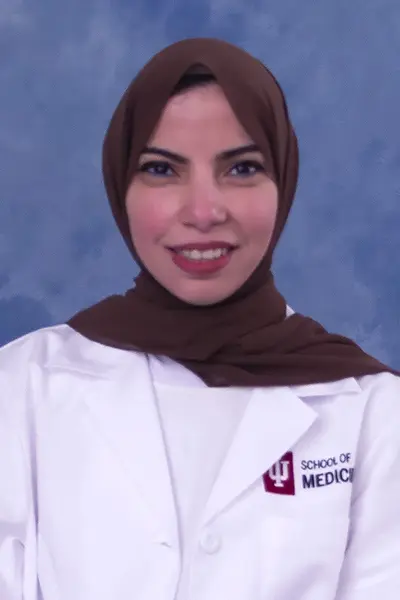 Reem wears a lab coat and brown head scarf