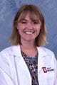 Devon wearing a lab coat and floral shirt. she has shoulder length light brown hair and a nose ring