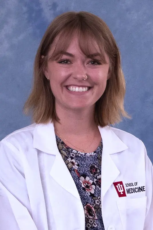 Devon wearing a lab coat and floral shirt. she has shoulder length light brown hair and a nose ring