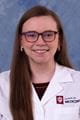 hannah wearing a lab coat with long brown hair and glasses