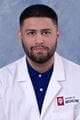 nabeel wearing a lab coat with short cropped dark hair and beard.