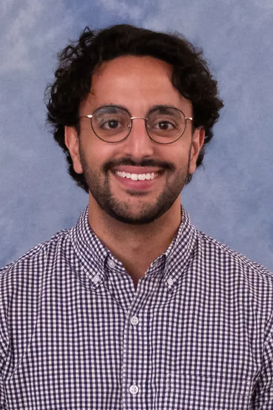 Patrick wearing a checkered shirt and glasses with dark curly hair and beard