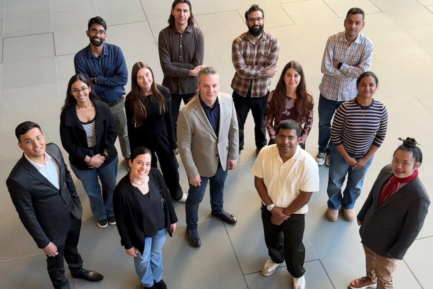 a diverse group of researchers stand on the ground floor and look up at the photographer taking their photo from above.
