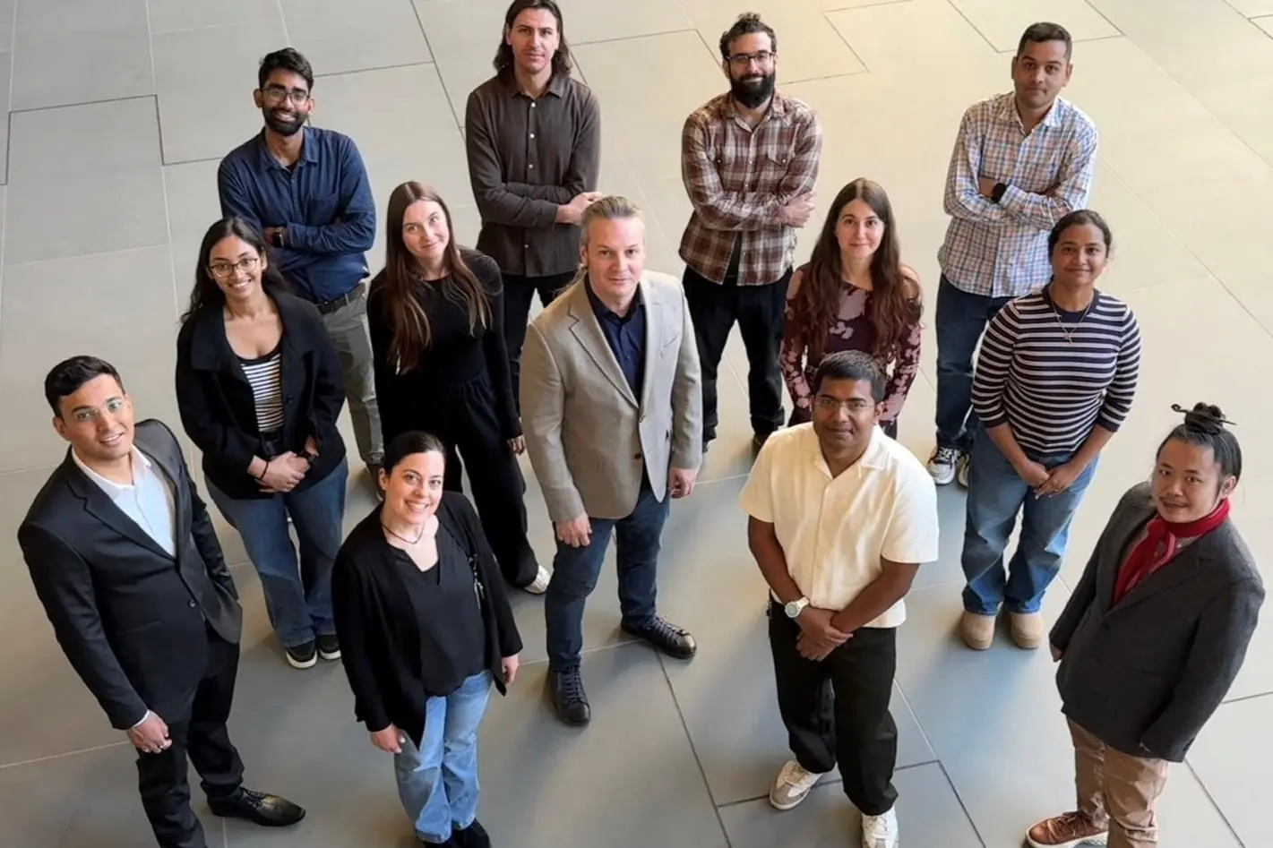 a diverse group of researchers stand on the ground floor and look up at the photographer taking their photo from above.