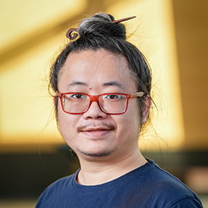 Suhang wearing his hair in a top knot with red-framed glasses