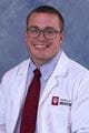 Eric wearing a white lab coat and tie with short cropped hair and glasses