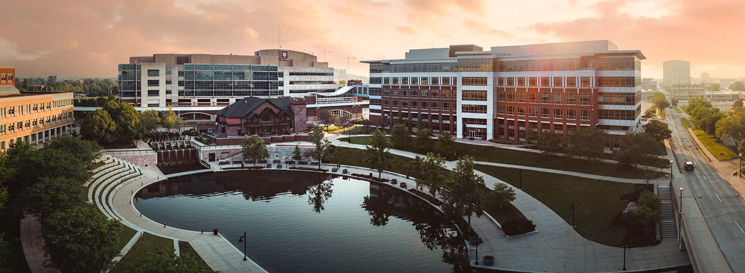 A serene aerial view of the IU School of Medicine campus at sunrise, featuring a reflective pond surrounded by modern architecture and lush greenery. The warm morning light enhances the campus's welcoming atmosphere, symbolizing a new day of discovery and learning.