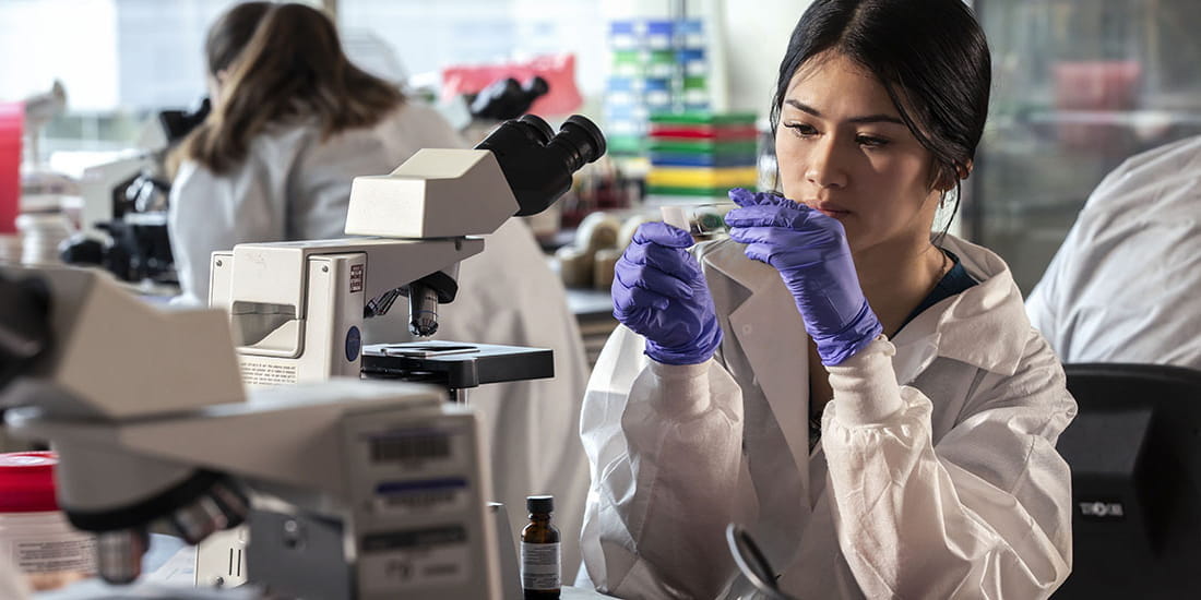 IU Pathology student looking at a lab slide by a microscope