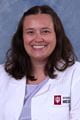 Kendall in a white lab coat. She has wavy dark brown hair falling over her shoulders.