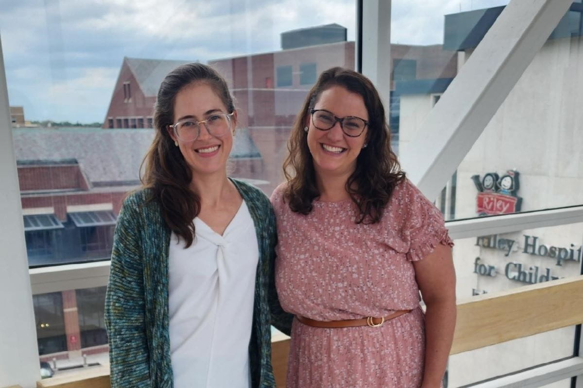 two women faculty members stand in front of a window overlooking Riley Hospital
