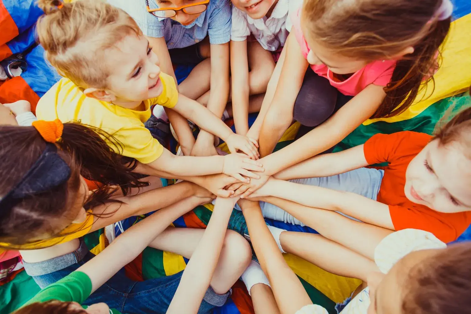 young kids all reach their hands into the middle of the circle