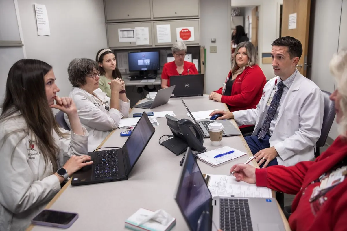 clinical staff discuss patient care together around a table in a hospital work room