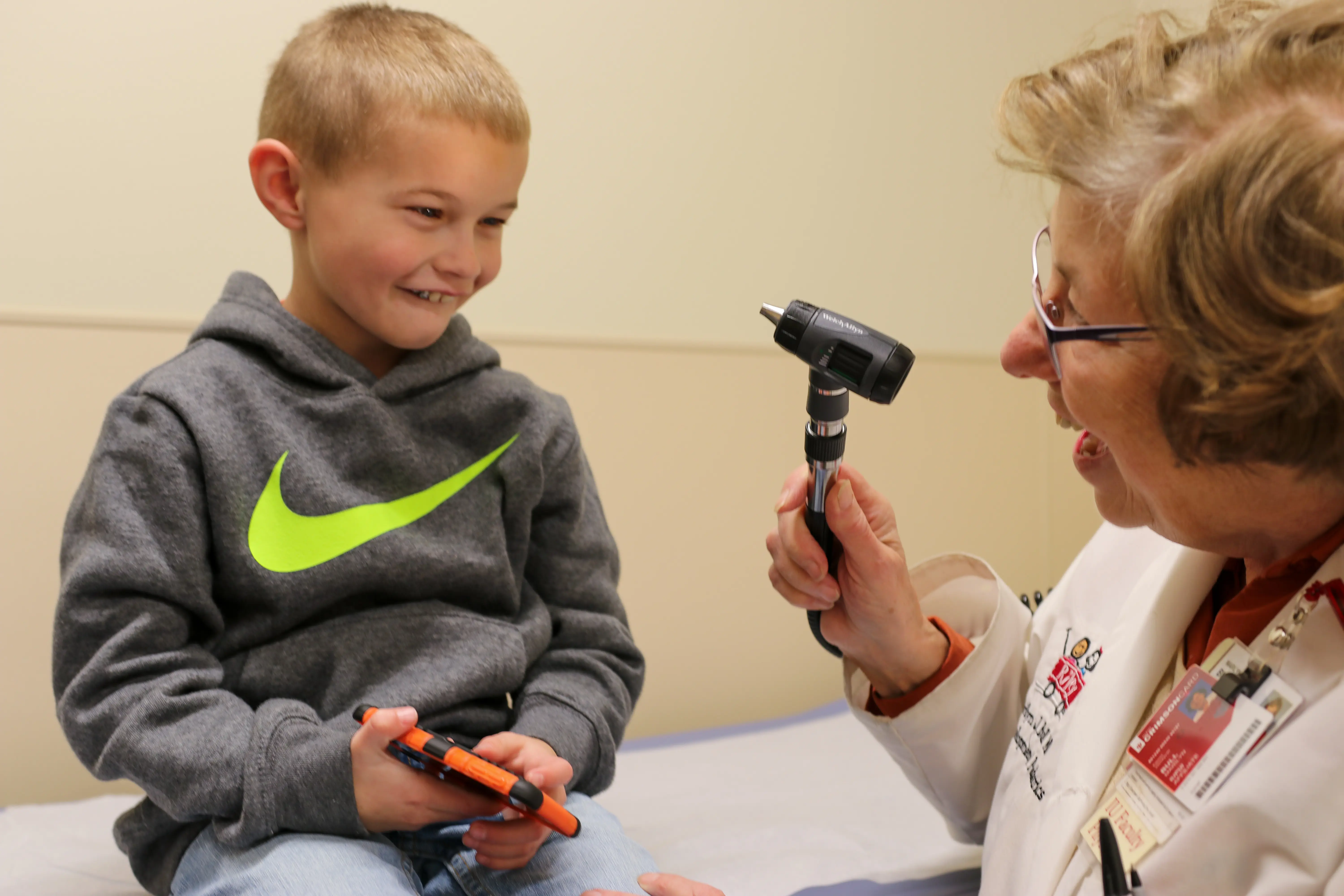 A young boy smiles at a doctor as she holds up a small light to examine his ears and throat