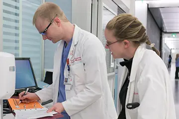 Two physicians wearing white coats in a hospital hallway while taking notes