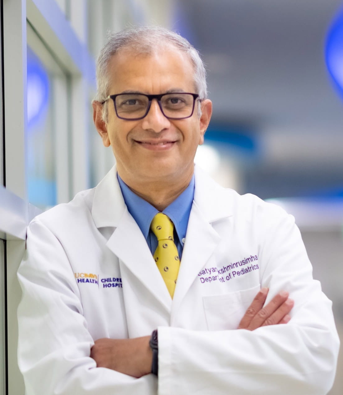 Headshot of a man with glasses in a white coat and tie