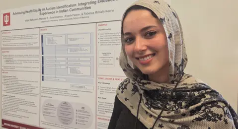 Malak Belkacemi, pursuing a pre-med track at IU, standing next to poster at Purdue Autism Conference