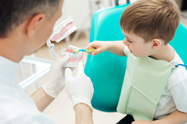 A young child practices toothbrushing on a model during a dental exam.