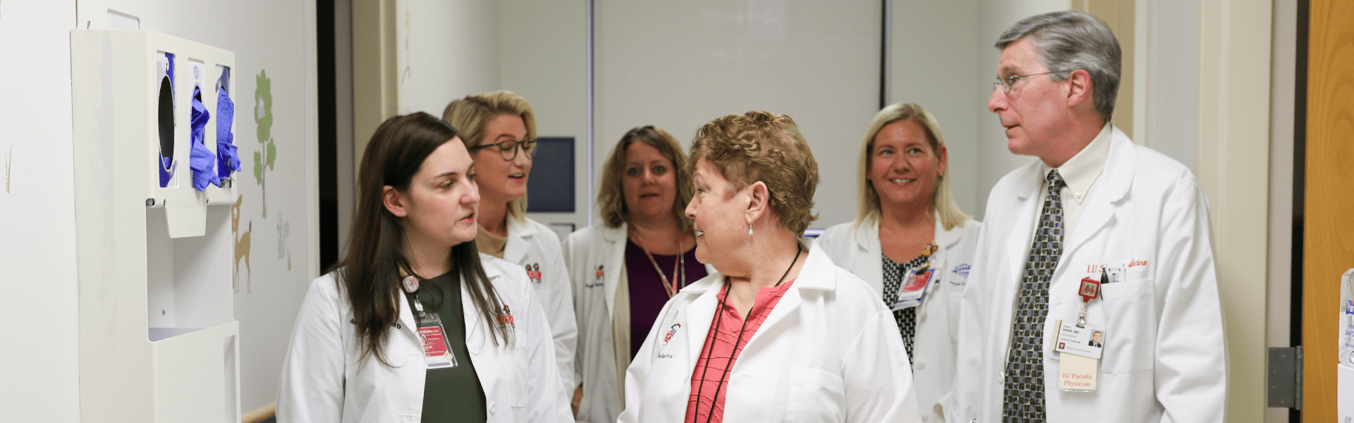 A group of six faculty physicians in white coats walk down the hall together while talking