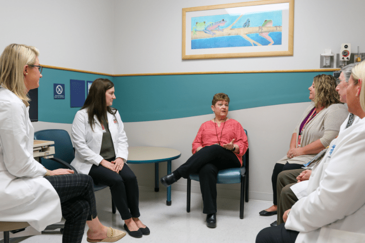 Six health care providers sit in a circle to talk about a case.