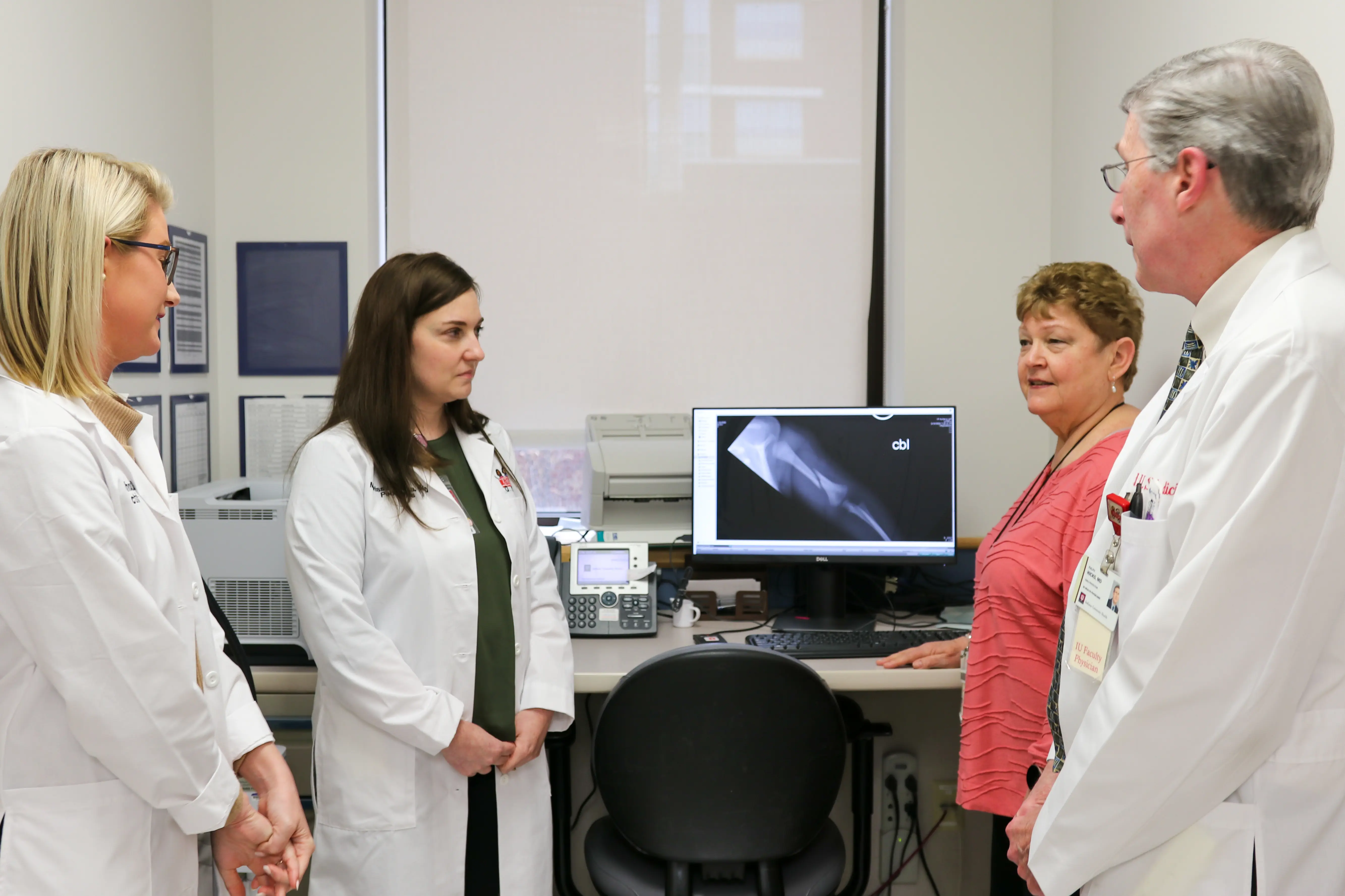 four faculty in white coats speak together in a work room in the hospital