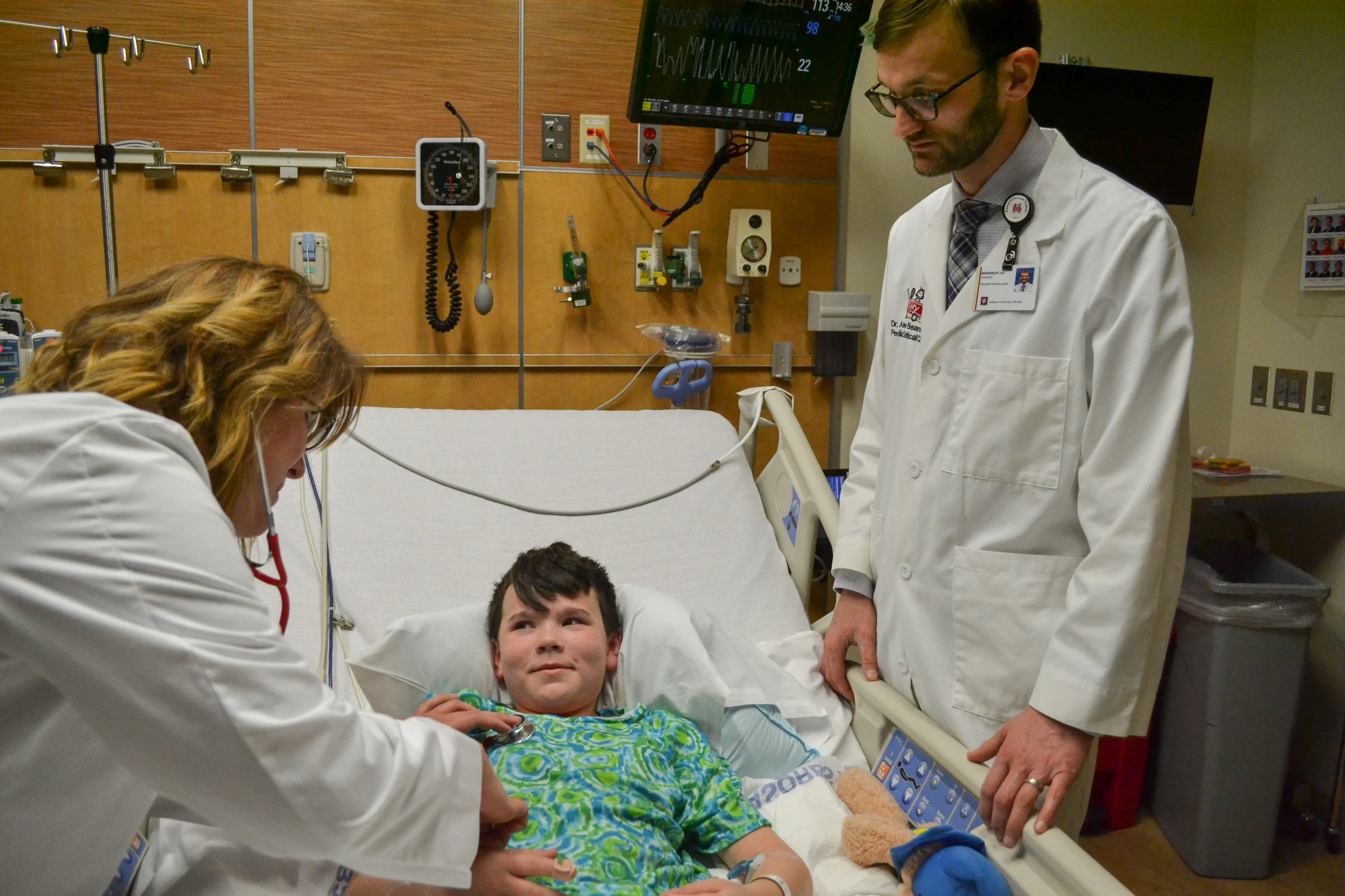 Two physicians in white coats examine a young patient in a hospital bed