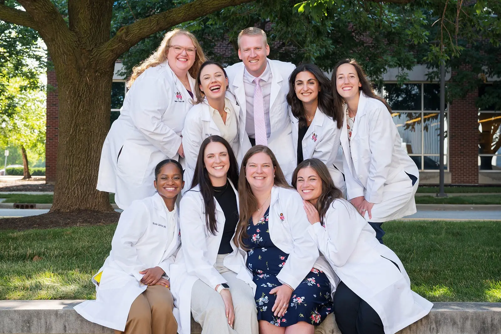 nine fellows in white coats cluster together and smile with their arms around each other