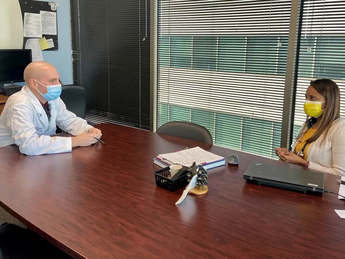Two endocrinology faculty chatting at a table several feet apart from each other while wearing masks.