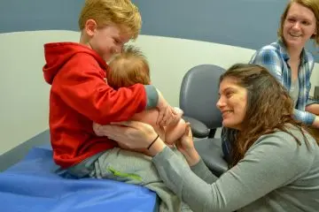 A member from the General and Community Pediatrics team consoling a smiling child holding his younger sibling.