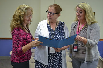 Three colleagues on the care team for the Center for Youth and Adults with Conditions of Childhood looking at content in a folder.