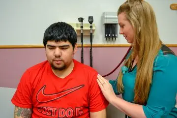 Teen male patient getting his breathing checked by a clinician in an exam room.