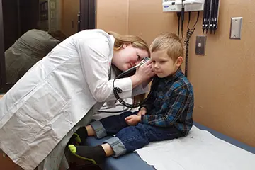 Pediatrician in a white coat checking the ears of a young boy