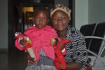 Woman hugging a young child holding two stuffed dolls