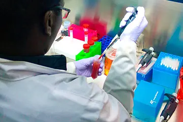 Up close view of a lab member pipetting a red liquid sample at a lab hood