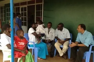 Doctors from the global health group sitting in chairs outside of a clinic chatting with patients